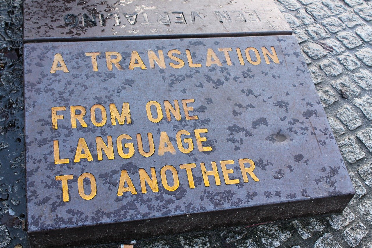 An artefact sculpted from stone, sitting on cobblestoned pavement. The inscription reads: A translation. From one language to another.