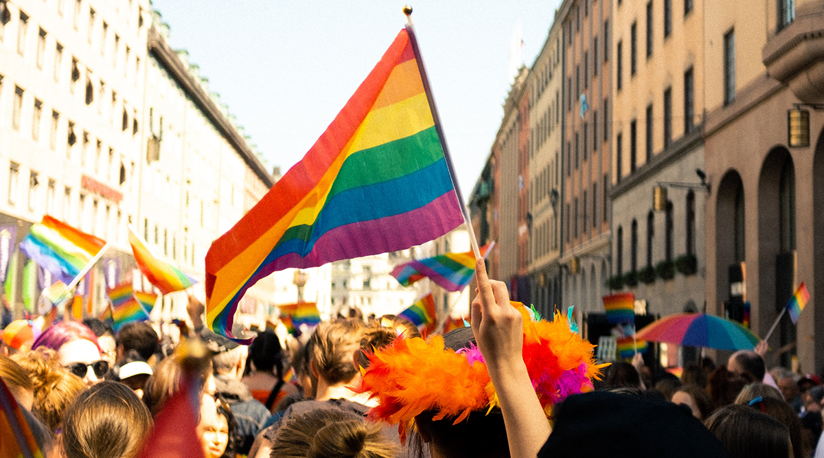 Image of a pride march with a pride flag held up at the centre. Photo by William Fonteneau on Unsplash