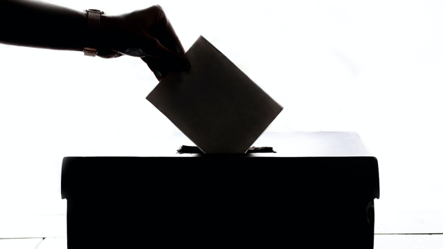 Silhouette image of a hand placing a slip of paper into a ballot box
