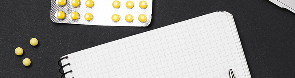 Blank notebook and yellow pills in their packet, along with three loose yellow pills