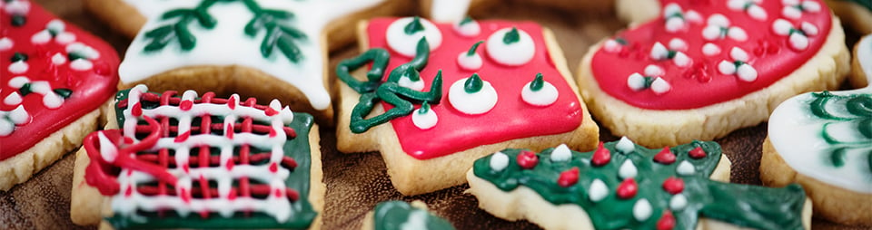 Close-up photograph of biscuits iced in a range of festive designs, with red, green and white icing - e.g. a gift, a christmas tree, a snowflake, a heart