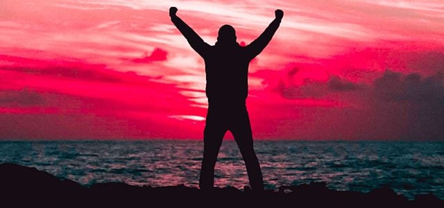 Silhouette of man raising arms against sunset