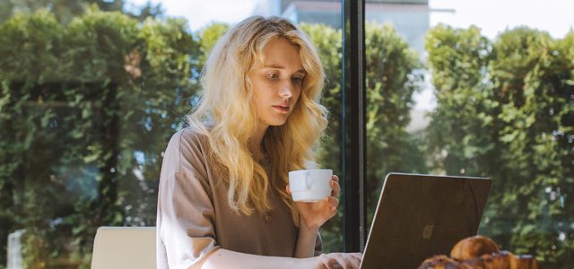 Woman holding coffee cuo as she types on laptop on table at home