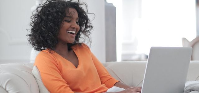 woman smiling at laptop while sitting on couch
