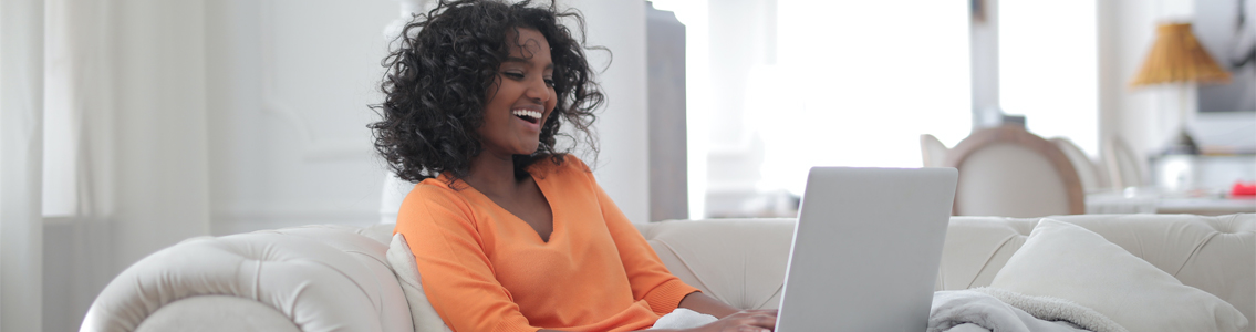 woman smiling at laptop while sitting on couch