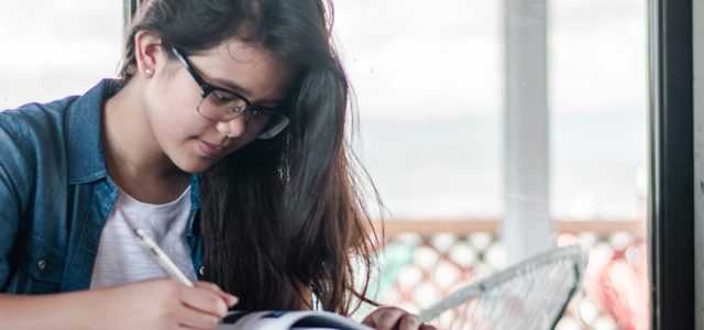 student taking notes while reading at desk at home