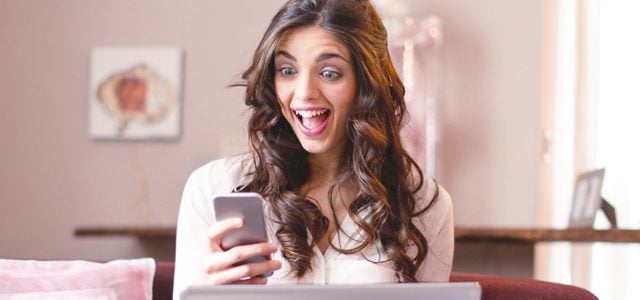 Woman looking surprised and happy while looking at phone and holding laptop
