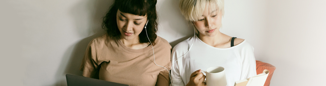 two women sharing headphones while each is reading
