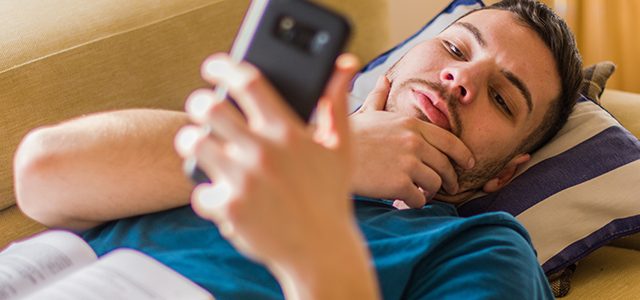 man lying on couch looking at phone