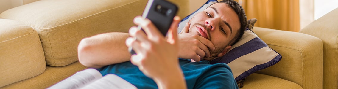 man lying on couch looking at phone