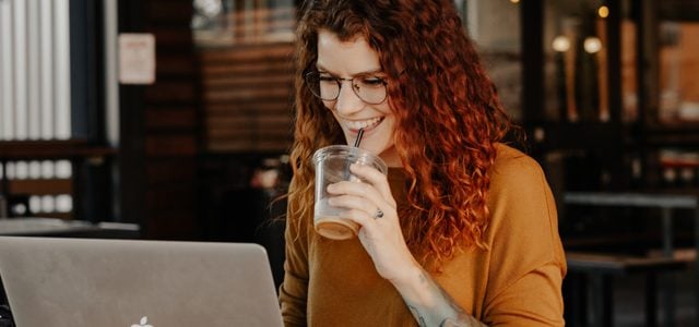 Woman smiling as she has a drink and works on laptop in cafe