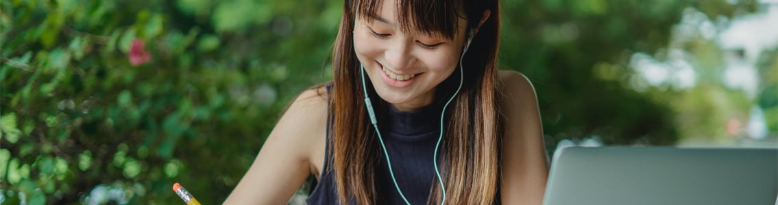 Smiling student wearing headphones while studying outside