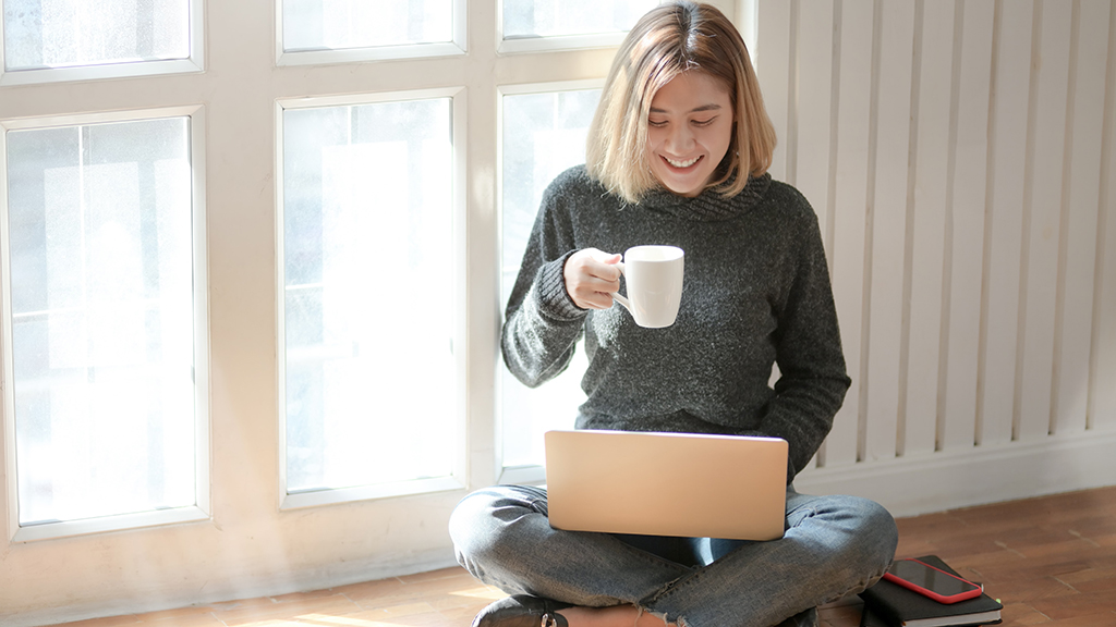 Smiling girl with mug sitting on floor with laptop