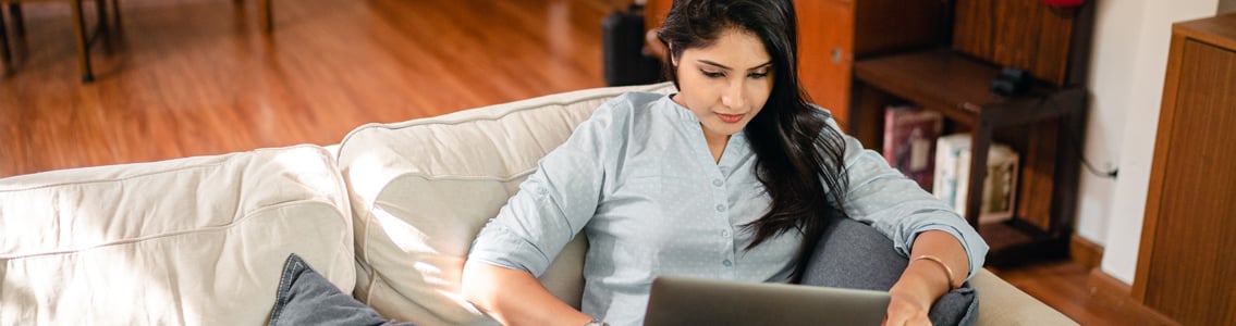 Woman studying on laptop while sitting on couch at home