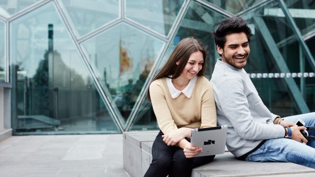 Two students smiling as they view tablet together
