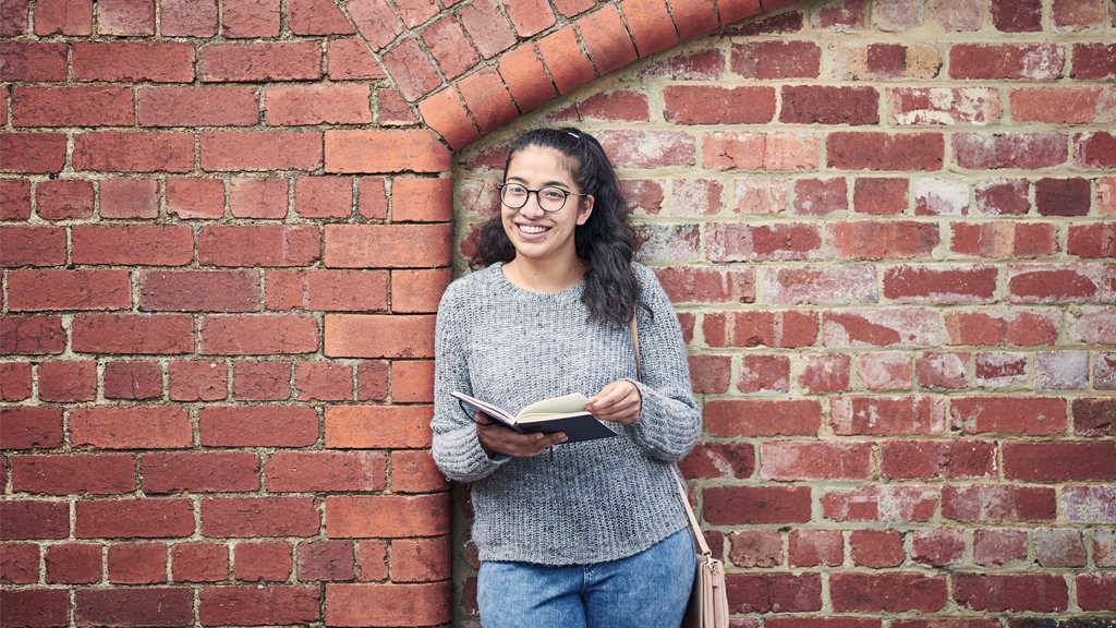 Student smiling as she refers to book outside at Waterfront Campus