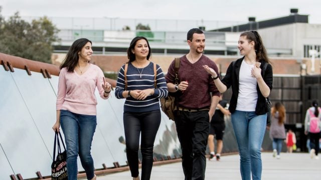 Four students talking as they walk across the footbridge at Burwood Campus