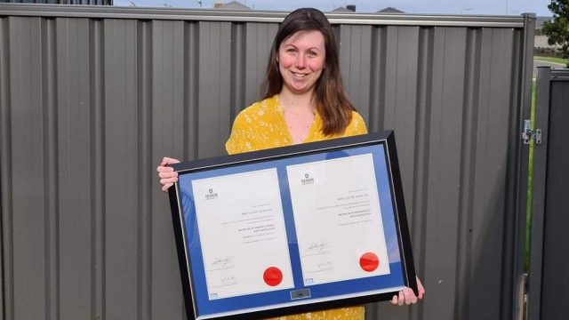 Peer mentor Amie holding her framed qualifications following graduation