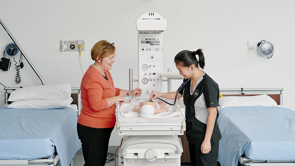 Nursing student examining baby with teacher