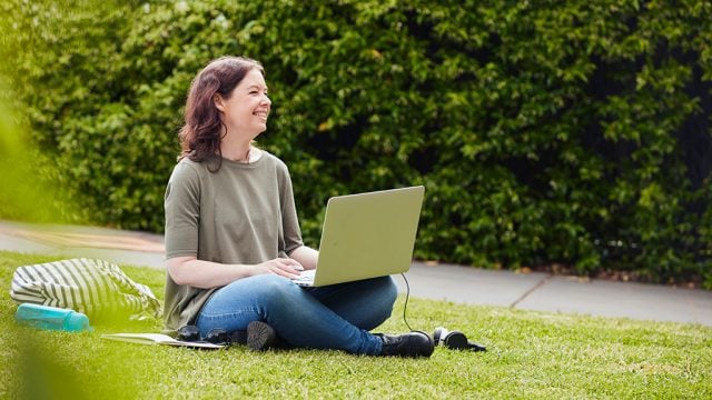 Smiling woman sitting on grass with laptop
