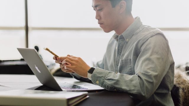 Student looking at mobile phone while seated at desk in front of laptop