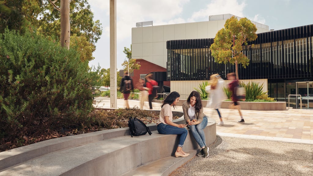Two students looking at phone while sitting outside at Burwood Campus