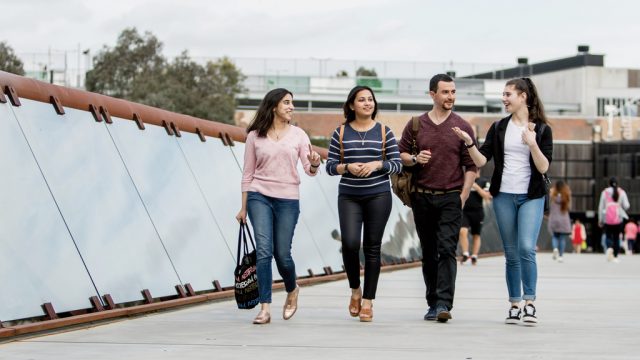 Four students chatting as they cross the footbridge at Burwood Campus