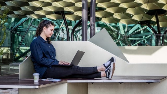 Student working on laptop while sitting on bench in Melbourne CBD