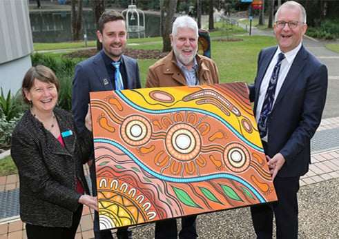 Deputy Vice-Chancellor of Education, Professor Liz Johnson, Indigenous Inclusion Coordinator Mr Tom Molyneux (Gunditjmara), Pro Vice-Chancellor of Indigenous Strategy and Innovation Professor Mark Rose (Gunditimara), and Vice-Chancellor Professor Iain Martin mark the milestone establishment of the VCIAC with the handover of an artwork painted by Nathan Patterson (Wagiman).