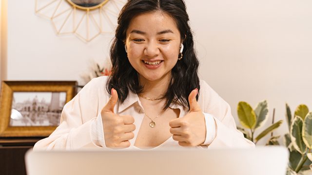 Smiling yougn woman giving thumbs up to a screen