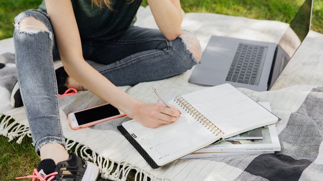 Cropped shot of woman with study materials sitting on grass