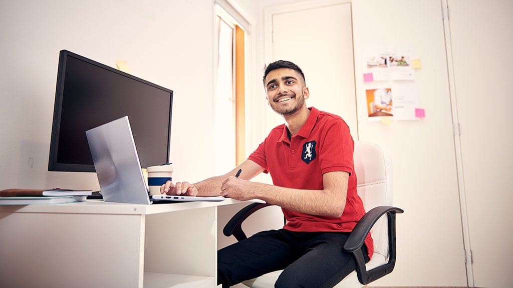 Smiling male student sitting at desk in bedroom