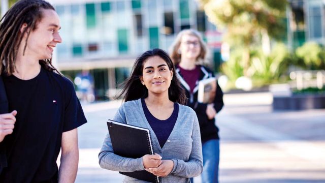 Student holding book and smiling as she walks through Burwood Campus with two friends