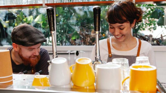 Two baristas smiling as they make coffees on machine