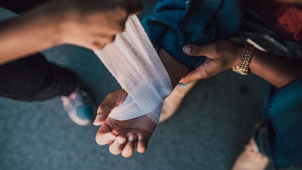 Close up view of person wrapping bandage around companion's hand and wrist