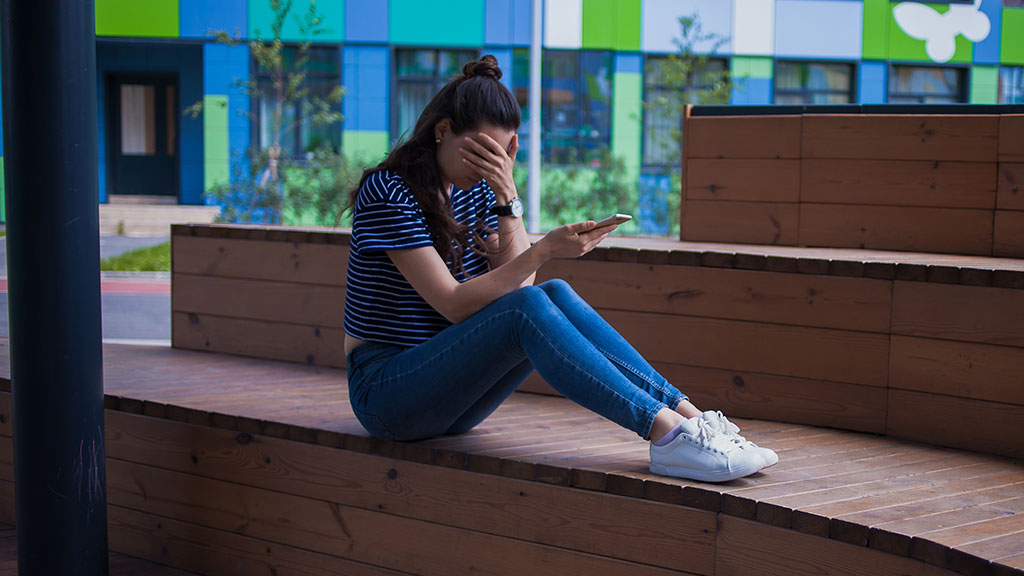 Distressed young woman sitting on bench with phone