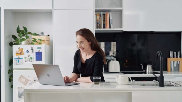 Woman typing on laptop at kitchen bench