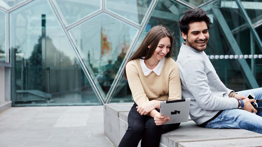 Young woman and man laughing as they look at tablet together outside at FedSquare in Melbourne