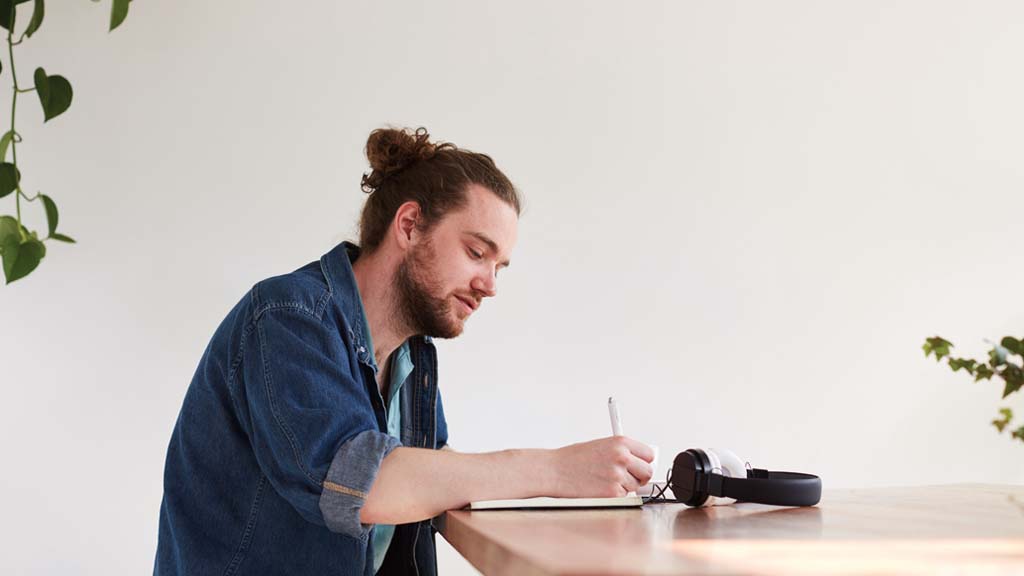 Man writing in notebook as he sits at desk
