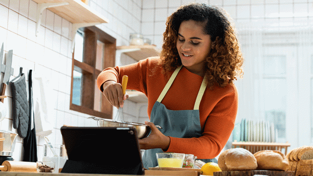 Smiling young woman cooking while watching tablet