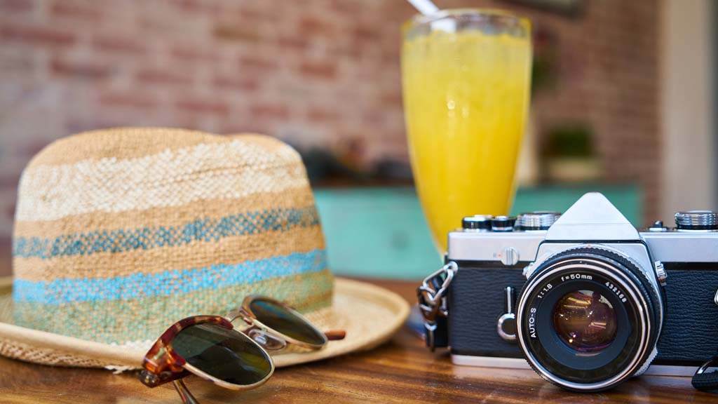Summer hat, sunglasses, camera and drink on table