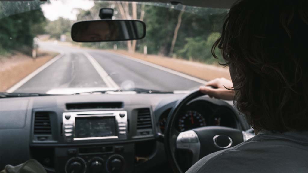 Man looking in rear-view mirror as he drives down rural road