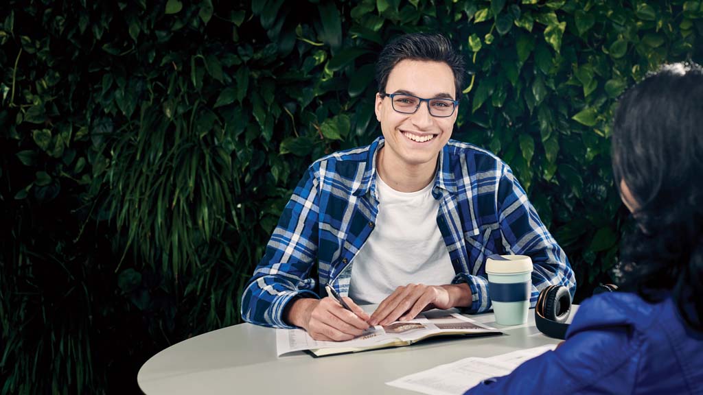 Male student smiling as he works outside with peer