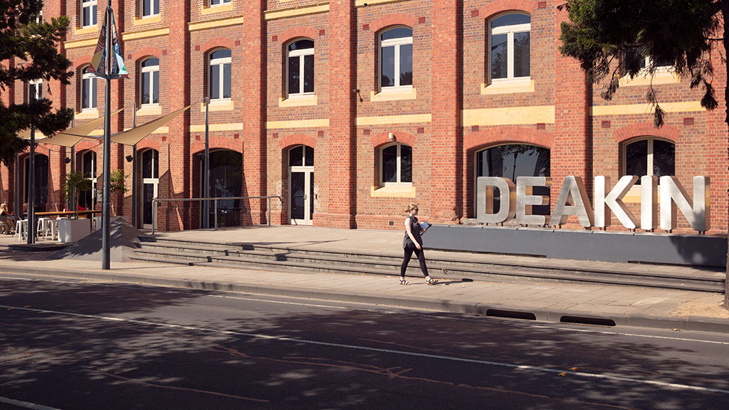 Female student walking past Deakin sign at Waterfront Campus