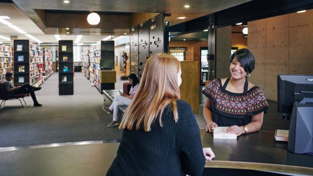 Student smiling as she chats to staff member in library
