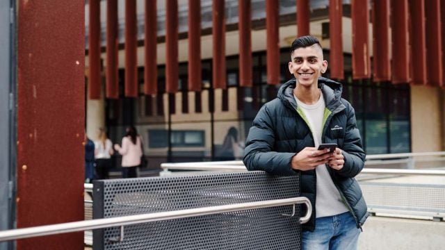 Student smiling while using mobile phone outside at Waurn Ponds Campus