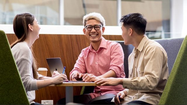 Three smiling students in group study space on campus