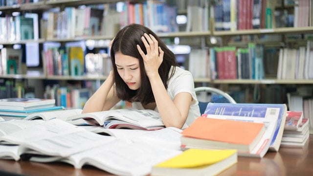 Stressed female student in library surrounded by books