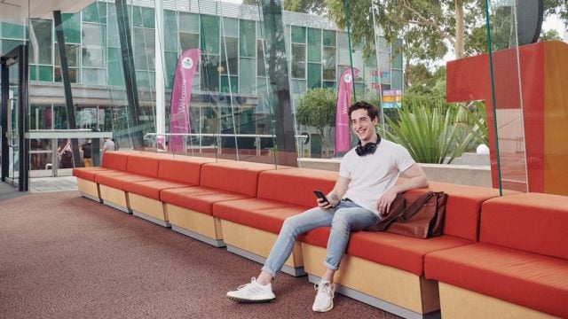 Student sitting on couch at Burwood Campus and smiling with mobile in hand