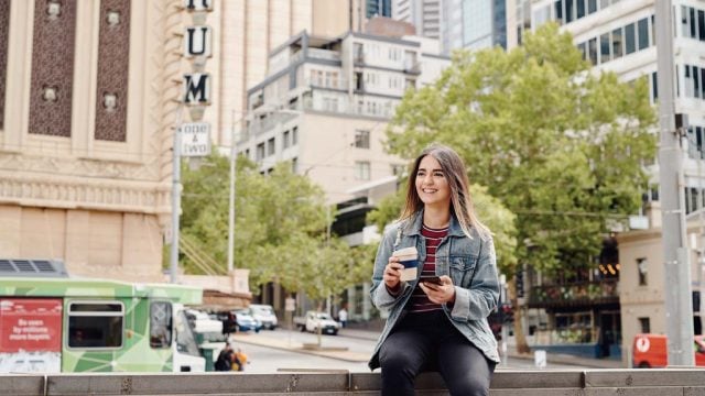 Student smiling as she looks at mobile phone while outside in Melbourne CBD